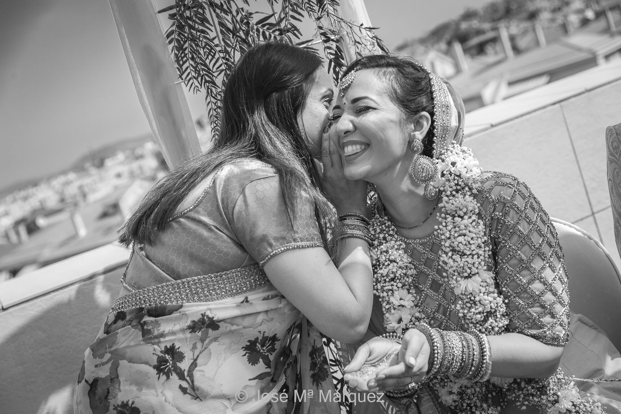 Ceremonia de Boda Hindú. Durante el Mehndi una amiga susurra consejos al oído a la novia. Reportajes de boda Hindú en Granada. Fotógrafo de Granada José María Márquez. parte de la ceremonia de las bodas hindúes se llama "Mehndi" o "Mehendi". Es una ceremonia prenupcial en la que las amigas y familiares cercanos de la novia le aplican henna en las manos y los pies, y le susurran consejos y bendiciones al oído mientras se lleva a cabo la aplicación. Es una celebración alegre y colorida que se realiza en la casa de la novia o en un lugar cercano a la boda.