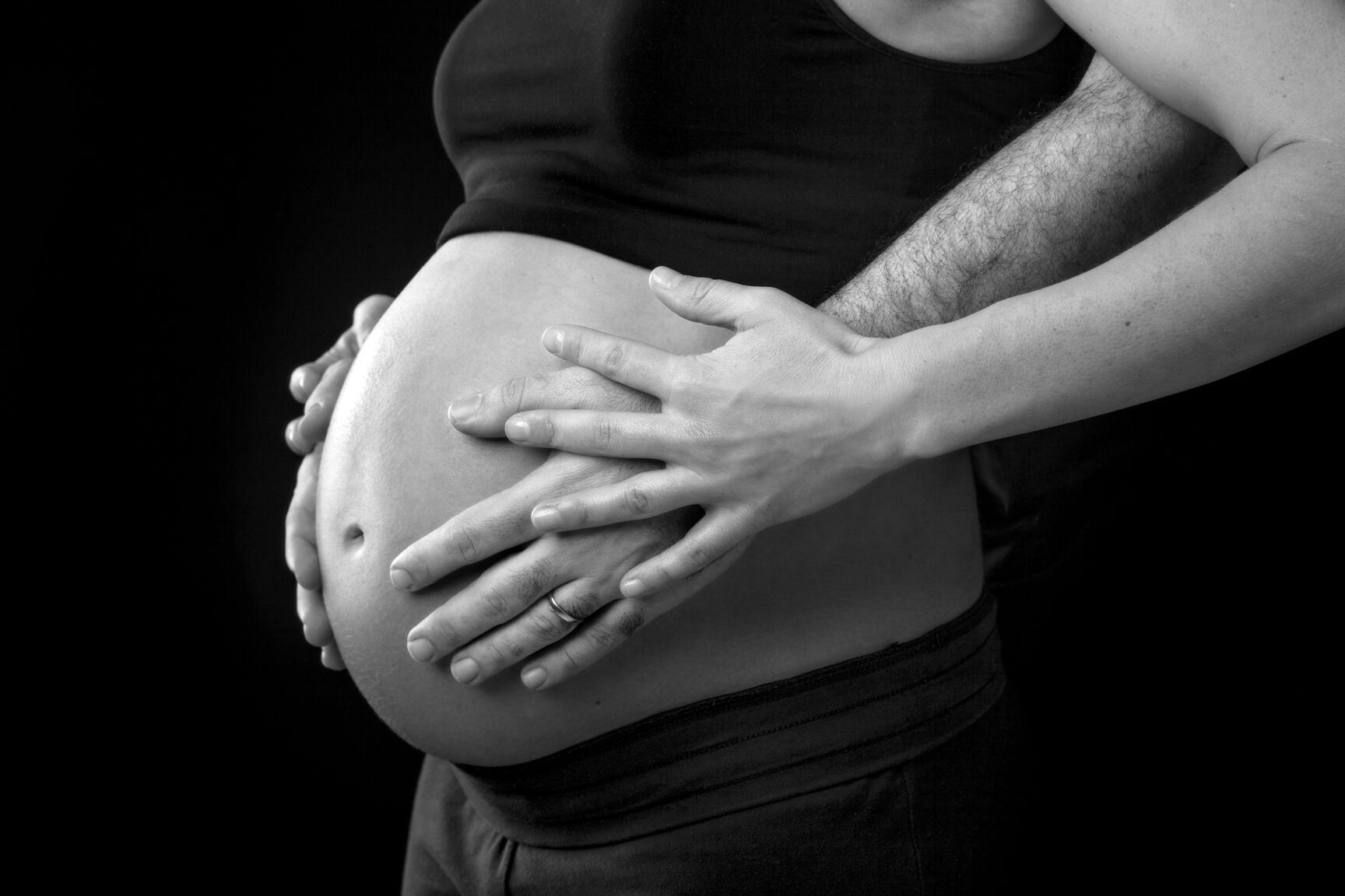 Detalle de las manos de la pareja en el vientre embarazado Plano detalle en blanco y negro de las manos de la pareja sobre el vientre de la futura mamá
