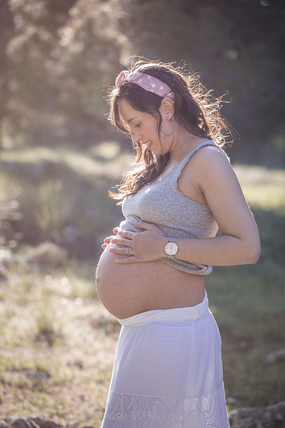 Plano medio de perfil de una chica embarazada en el campo. La chica se mira y acaricia el vientre mientras la luz del atardecer acentúa la silueta embarazada