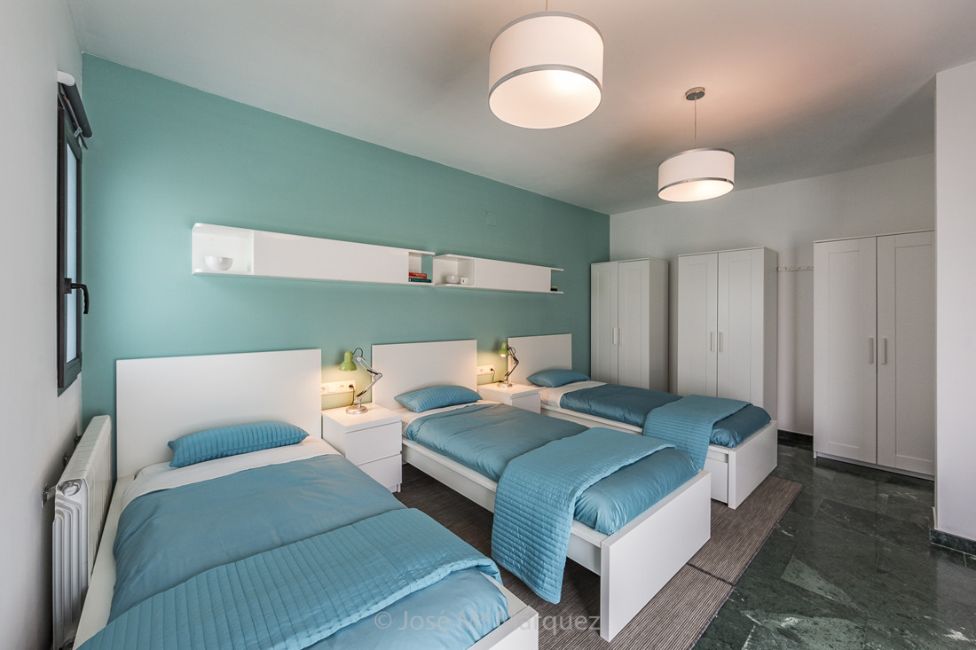 Dormitorio con tres camas decorado en blanco y verde agua. Reportaje publicitarío en Granada. Fotos empresas