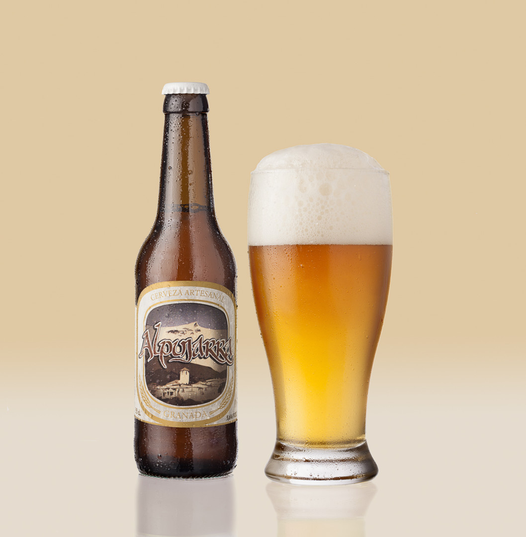 Fotografía de bebidas y productos alimenticios. Cerveza artesanal ALPUJARRA y copa de cerveza con espuma. Efecto de frío con gotitas de condensación de agua